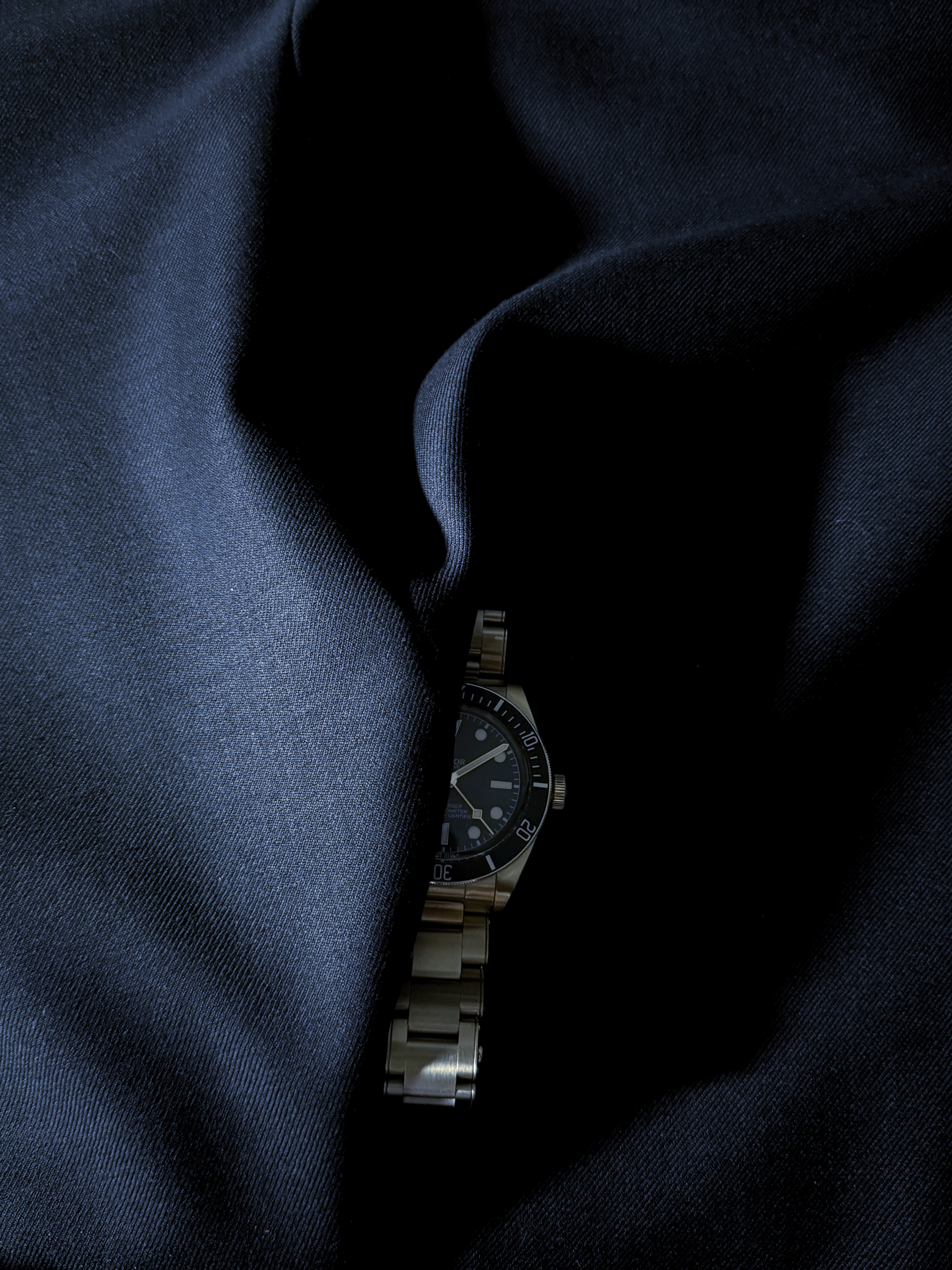 A navy dive watch partially concealed within folds of dark navy cloth